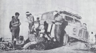 YNK229F sank through the crust in the salt desert in Iran - the Dasht-e Lut . After 24 hours digging the truck still could not be extracted. Eventually, a tractor was found to pull it out. Standing on the left is Stuart Jenkins eating beans from a can, Larry Weiss is standing next to Stuart and on the far right is Larry, a freelance photographer from the USA. Clive Imrie is seated in the back of the truck.